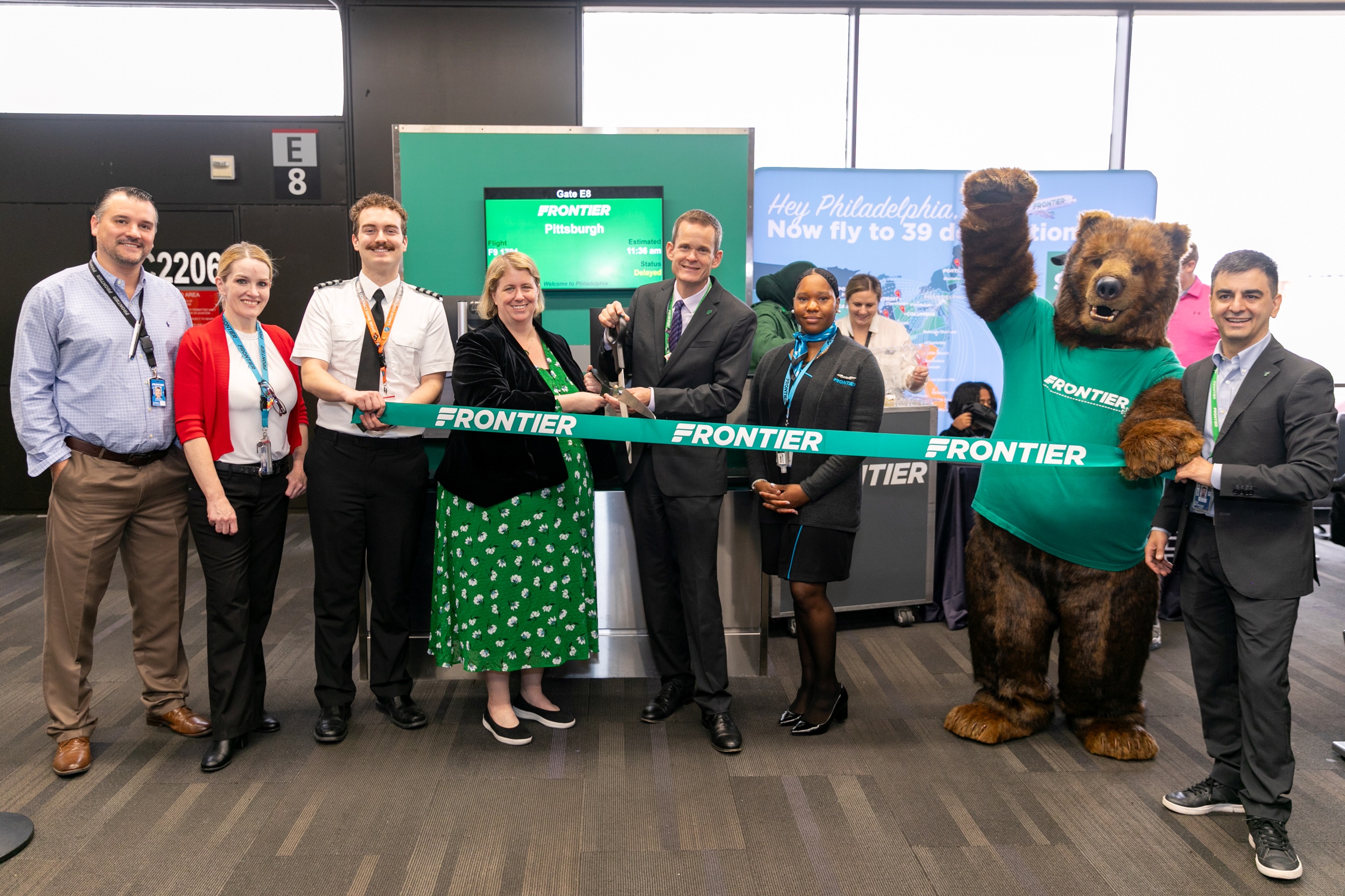 Group cutting green frontier ribbon with brown bear mascot.