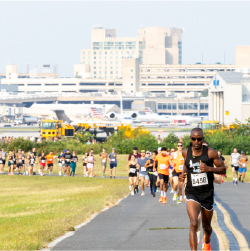 runners racing on the runway with the airport in background