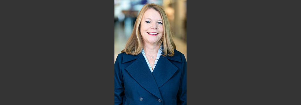 Denise-blone hair, blue eyes, navy blue double-breasted suit jacket. Blurred airport background