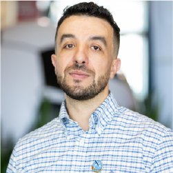 Man with dark hair, beard and blue checkered button up shirt