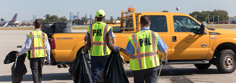employees in neon vests, with trash bags on airfield
