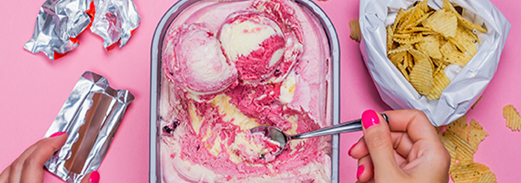 person hands picking up ice cream with spoon and chips and candy on the side