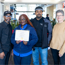 Touree posing with coworkers while holding certificate